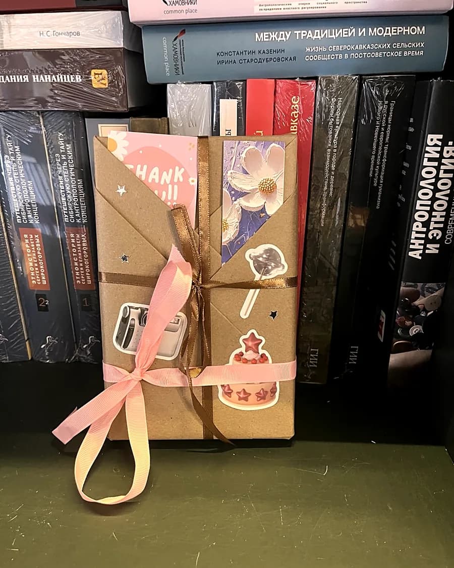 Книга вслепую в крафтовой обёртке с лентой и стикерами среди книжных стопок